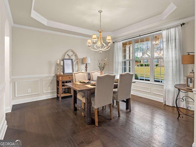 dining room featuring ornamental molding, dark wood-type flooring, a tray ceiling, and a chandelier