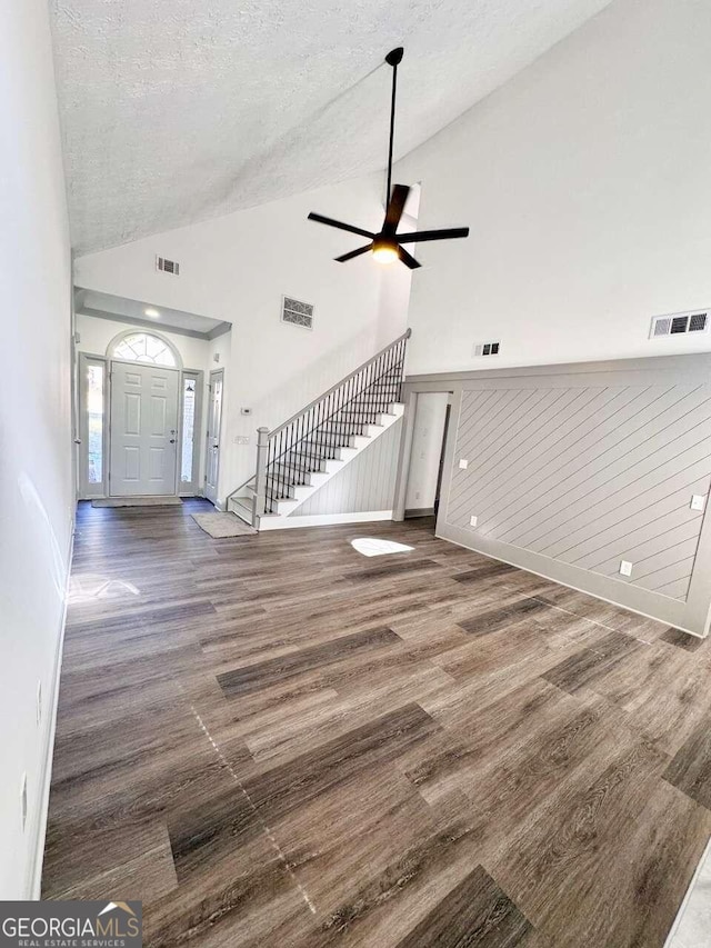 unfurnished living room with dark hardwood / wood-style flooring, a textured ceiling, high vaulted ceiling, and wood walls