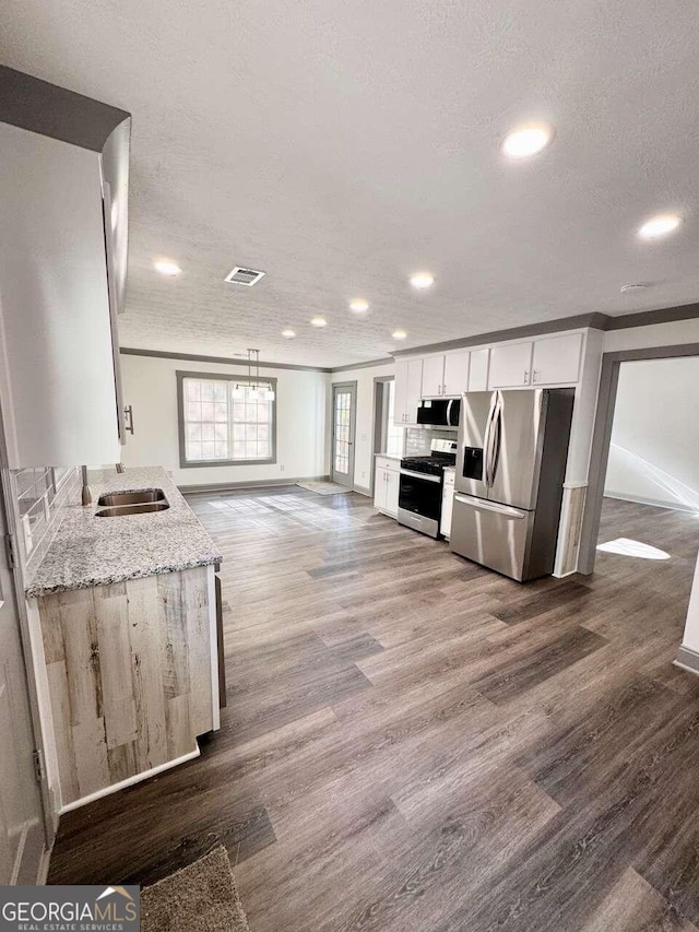 kitchen with light stone countertops, a textured ceiling, stainless steel appliances, hardwood / wood-style flooring, and white cabinets