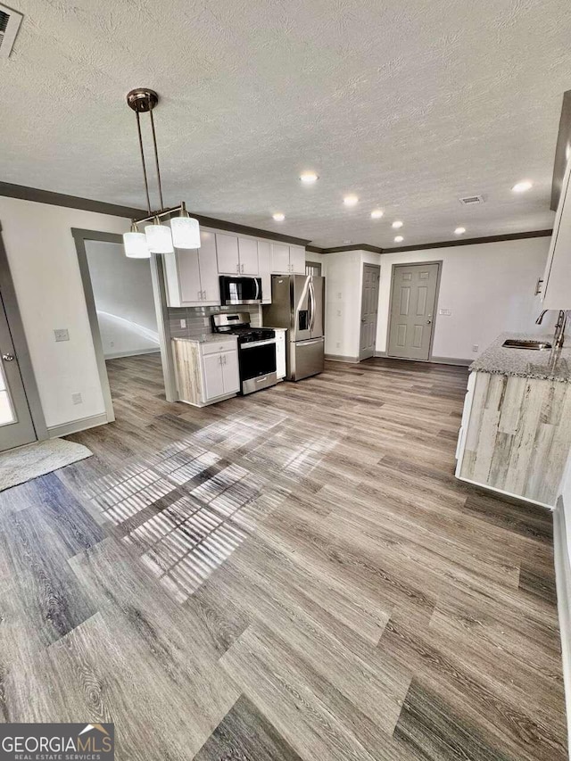 kitchen featuring appliances with stainless steel finishes, sink, white cabinets, light hardwood / wood-style floors, and hanging light fixtures