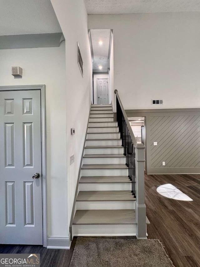 staircase featuring wood-type flooring, a textured ceiling, and wood walls