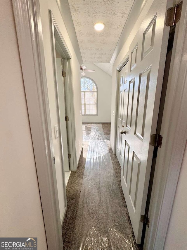 hall featuring dark carpet and a textured ceiling