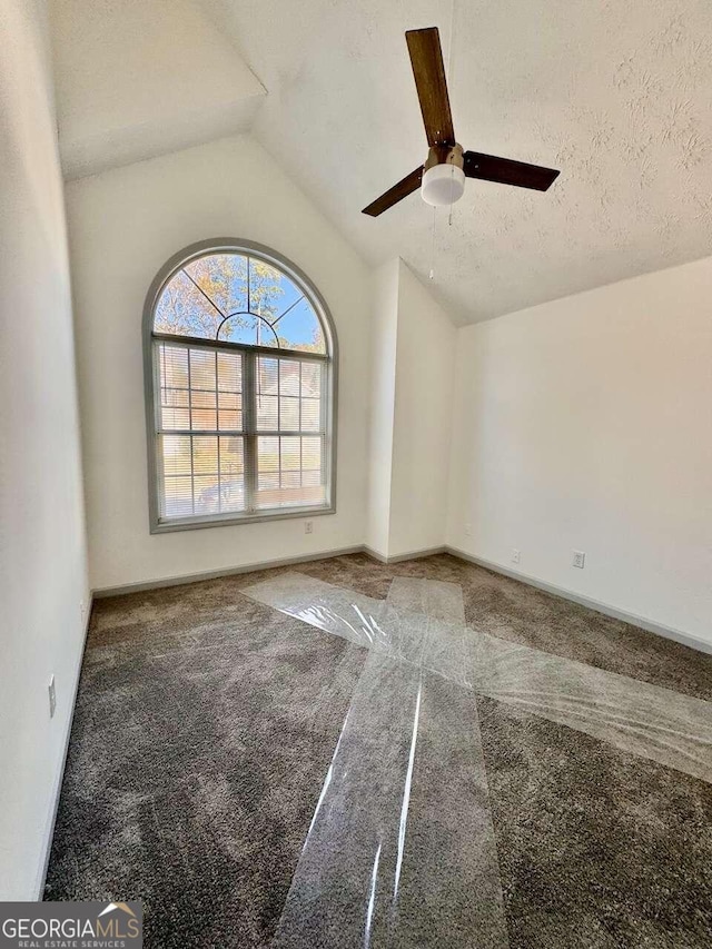 empty room with a textured ceiling, carpet floors, ceiling fan, and lofted ceiling