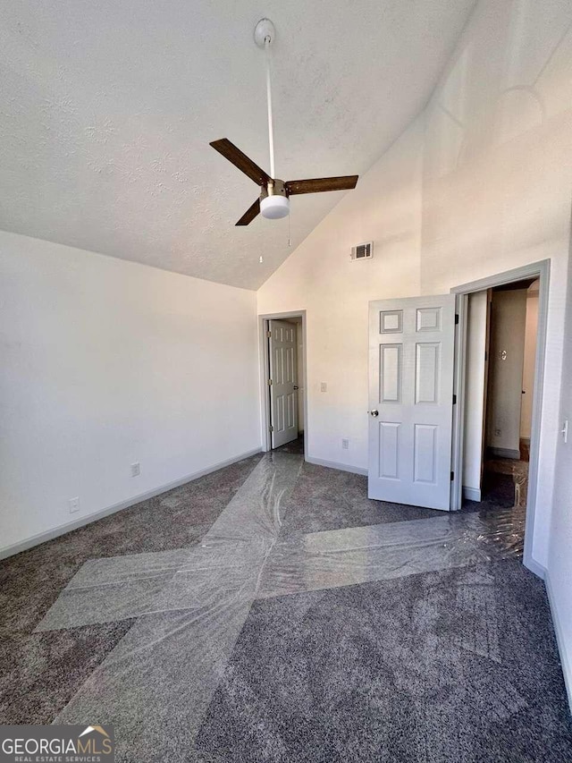 unfurnished bedroom with a textured ceiling, high vaulted ceiling, dark carpet, and ceiling fan