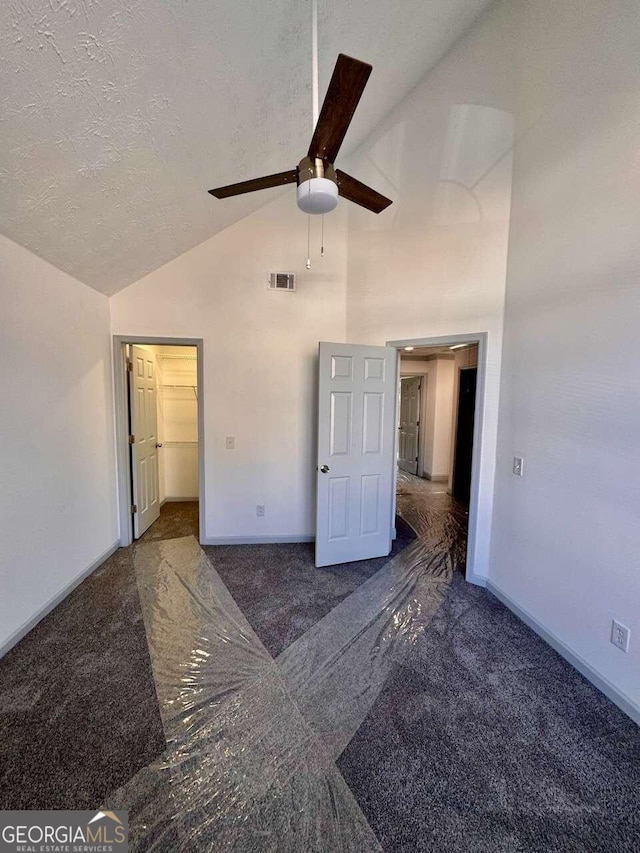 unfurnished bedroom featuring dark carpet, ceiling fan, a spacious closet, a textured ceiling, and a closet