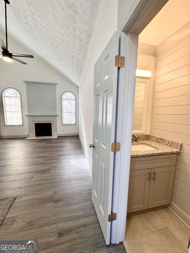 corridor with a textured ceiling, sink, light hardwood / wood-style floors, and vaulted ceiling