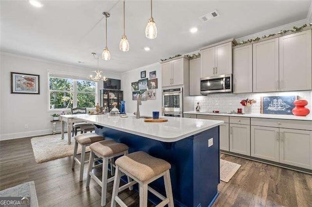 kitchen with appliances with stainless steel finishes, a center island with sink, gray cabinets, and pendant lighting