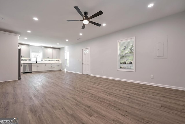 unfurnished living room featuring electric panel, dark hardwood / wood-style floors, ceiling fan, and sink