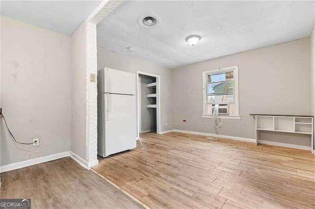 unfurnished bedroom featuring cooling unit, a closet, white fridge, and light wood-type flooring