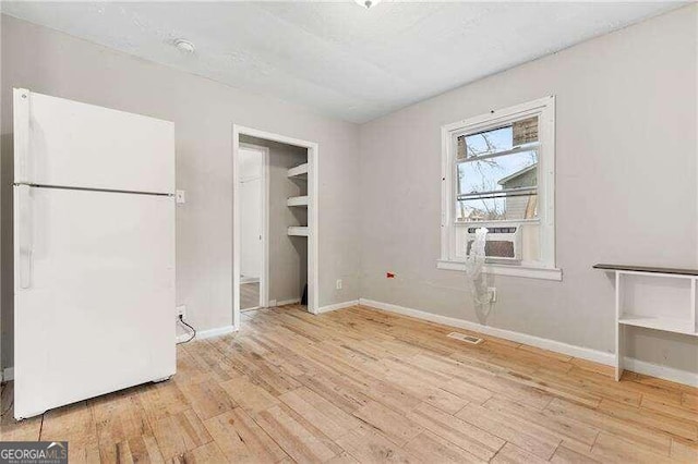 unfurnished bedroom featuring cooling unit, a walk in closet, white fridge, and light wood-type flooring