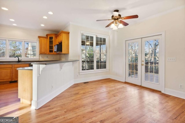 kitchen featuring ceiling fan, french doors, light hardwood / wood-style flooring, crown molding, and a breakfast bar area