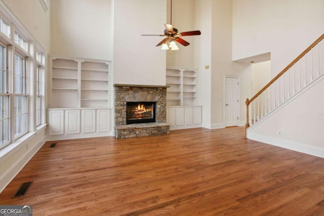 unfurnished living room featuring built in shelves, ceiling fan, a high ceiling, a fireplace, and hardwood / wood-style flooring