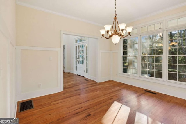 unfurnished dining area with wood-type flooring, crown molding, and a chandelier