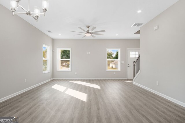 unfurnished living room with hardwood / wood-style flooring, ceiling fan with notable chandelier, and a healthy amount of sunlight