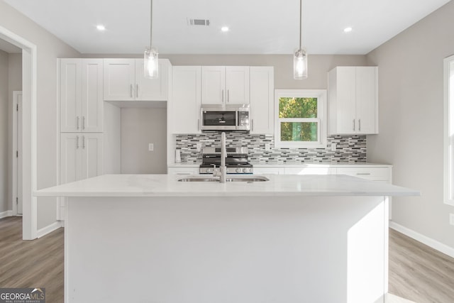 kitchen with sink, light stone counters, a kitchen island with sink, white cabinets, and appliances with stainless steel finishes