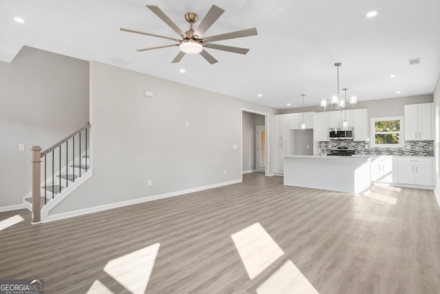 unfurnished living room featuring ceiling fan with notable chandelier and light hardwood / wood-style floors