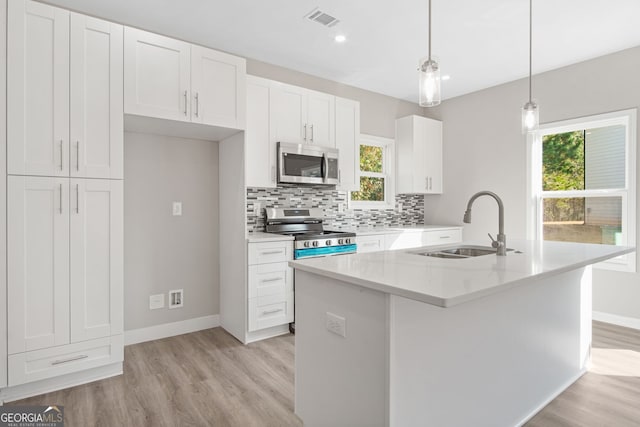 kitchen featuring hanging light fixtures, stainless steel appliances, white cabinets, and a kitchen island with sink