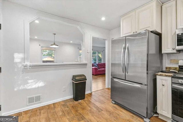 kitchen with a wealth of natural light, decorative light fixtures, light wood-type flooring, and appliances with stainless steel finishes