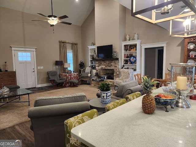 living room featuring ceiling fan with notable chandelier, a fireplace, high vaulted ceiling, and dark wood-type flooring