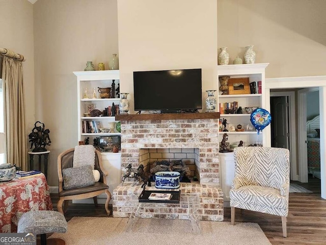 living room featuring wood-type flooring, a towering ceiling, and a brick fireplace