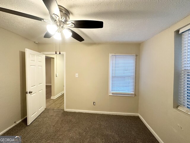 spare room with a wealth of natural light, dark carpet, and a textured ceiling