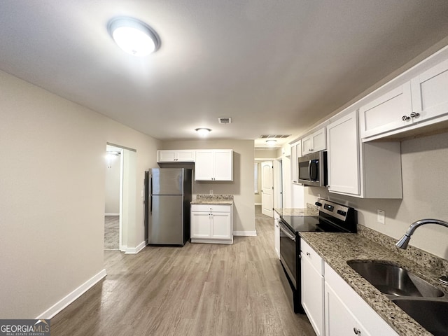 kitchen with white cabinets, sink, appliances with stainless steel finishes, light hardwood / wood-style floors, and light stone counters