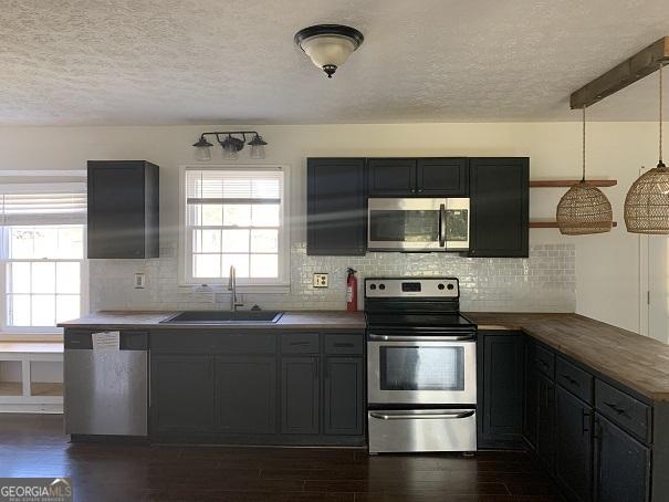 kitchen with sink, tasteful backsplash, dark hardwood / wood-style floors, pendant lighting, and appliances with stainless steel finishes