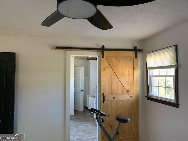 exercise room featuring hardwood / wood-style flooring, ceiling fan, a barn door, and a textured ceiling