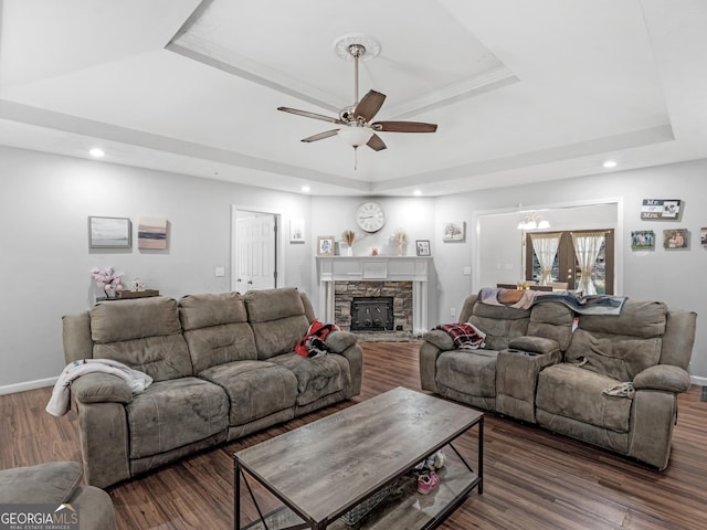 living room featuring french doors, a stone fireplace, dark hardwood / wood-style floors, a tray ceiling, and ceiling fan with notable chandelier