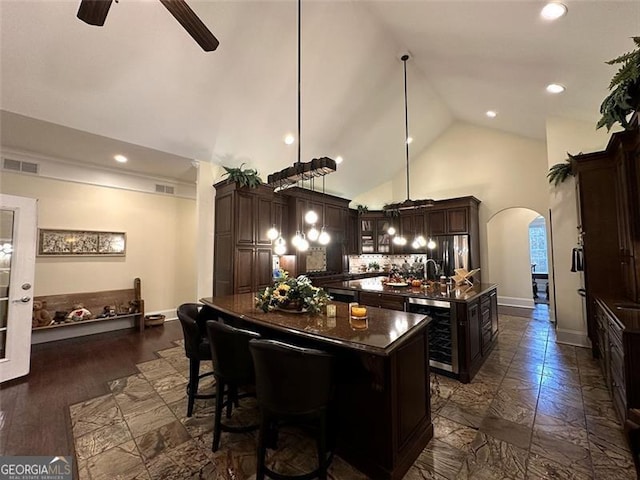 kitchen featuring ceiling fan, wine cooler, decorative light fixtures, a kitchen island with sink, and dark brown cabinets