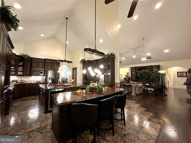 kitchen with pendant lighting, dark wood-type flooring, ceiling fan, appliances with stainless steel finishes, and a kitchen island