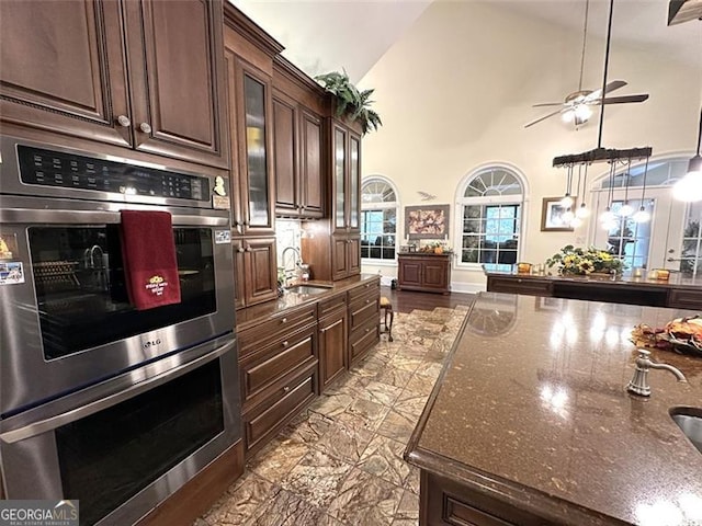 kitchen featuring dark brown cabinetry, sink, high vaulted ceiling, double oven, and dark stone counters