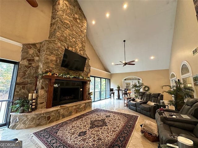 living room featuring a wealth of natural light, ceiling fan, a stone fireplace, and high vaulted ceiling