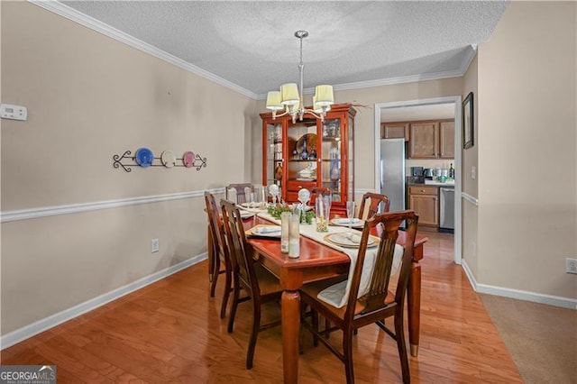 dining room with a textured ceiling, a notable chandelier, light hardwood / wood-style floors, and crown molding