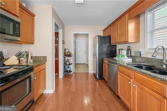 kitchen featuring dark stone counters, sink, appliances with stainless steel finishes, and light hardwood / wood-style flooring