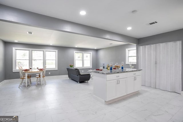 kitchen with light stone countertops, a center island, and white cabinetry