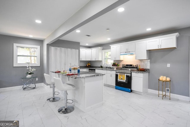 kitchen with stainless steel range with electric stovetop, white cabinetry, backsplash, and a breakfast bar area