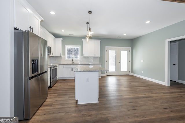 kitchen with decorative light fixtures, a kitchen island, white cabinets, and appliances with stainless steel finishes