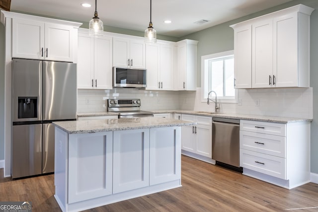 kitchen featuring stainless steel appliances, sink, white cabinets, and decorative light fixtures