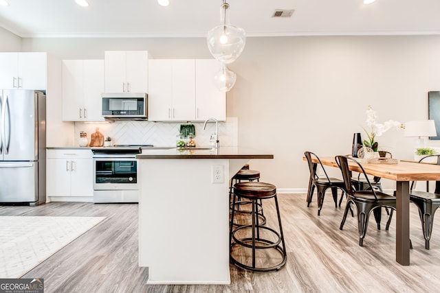 kitchen featuring appliances with stainless steel finishes, light hardwood / wood-style floors, white cabinetry, and hanging light fixtures