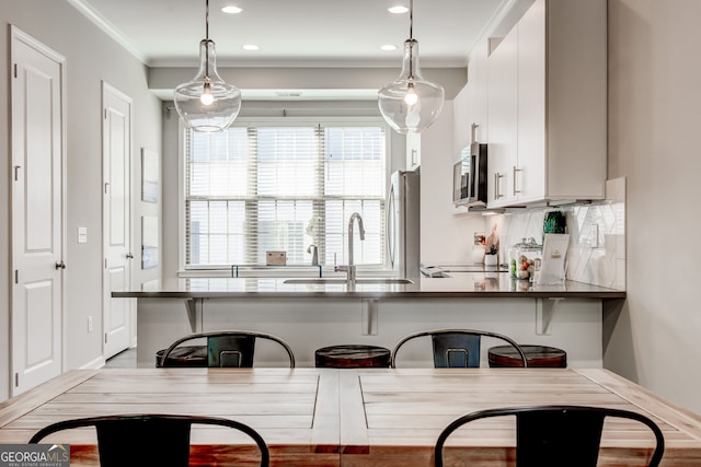 kitchen with white cabinets, decorative light fixtures, a kitchen bar, and stainless steel appliances