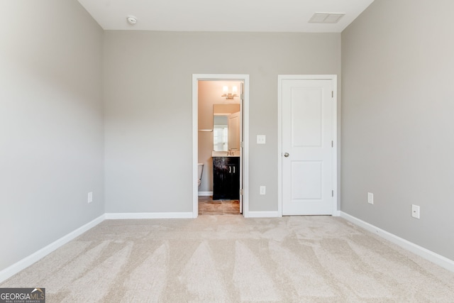 unfurnished bedroom featuring ensuite bathroom and light carpet