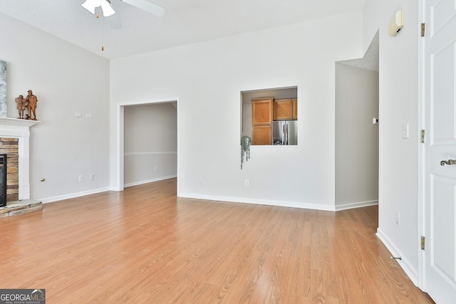 unfurnished living room with a textured ceiling, light hardwood / wood-style floors, a stone fireplace, and ceiling fan