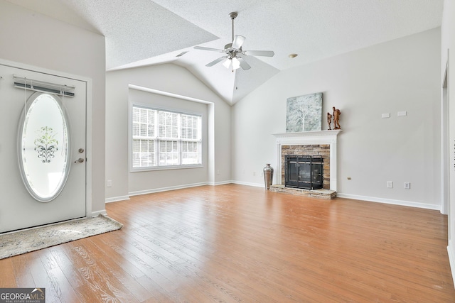 unfurnished living room featuring ceiling fan, a stone fireplace, light hardwood / wood-style flooring, a textured ceiling, and lofted ceiling