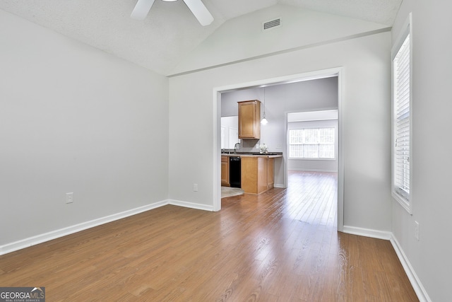 unfurnished living room featuring a textured ceiling, light hardwood / wood-style floors, vaulted ceiling, and ceiling fan