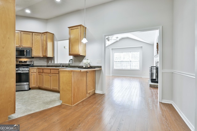 kitchen featuring stainless steel appliances, a brick fireplace, pendant lighting, lofted ceiling, and light wood-type flooring