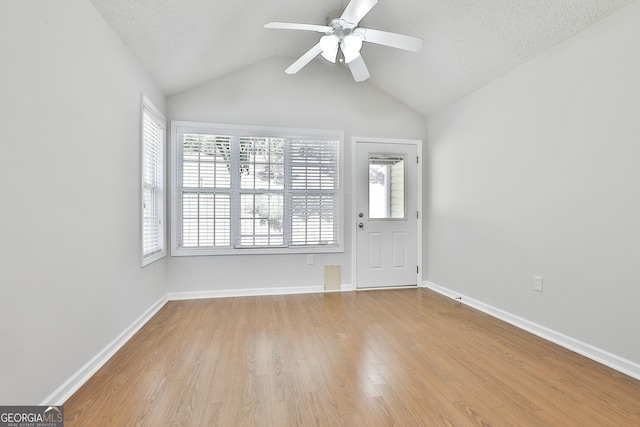 spare room featuring ceiling fan, light wood-type flooring, lofted ceiling, and a textured ceiling