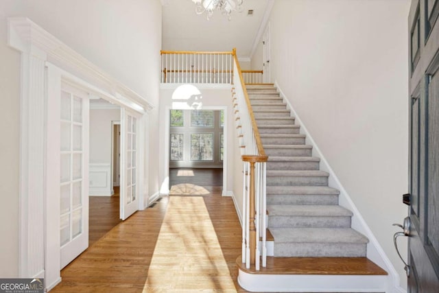 foyer entrance featuring french doors, light wood-type flooring, ornamental molding, a towering ceiling, and a notable chandelier