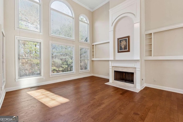 unfurnished living room with dark hardwood / wood-style flooring, built in features, plenty of natural light, and crown molding