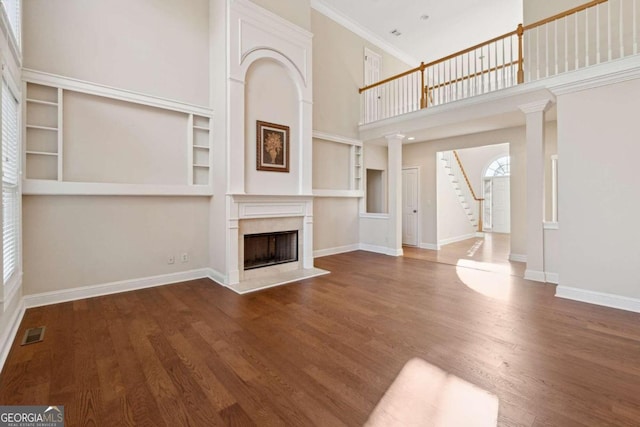 unfurnished living room featuring ornamental molding, a towering ceiling, built in features, and dark wood-type flooring